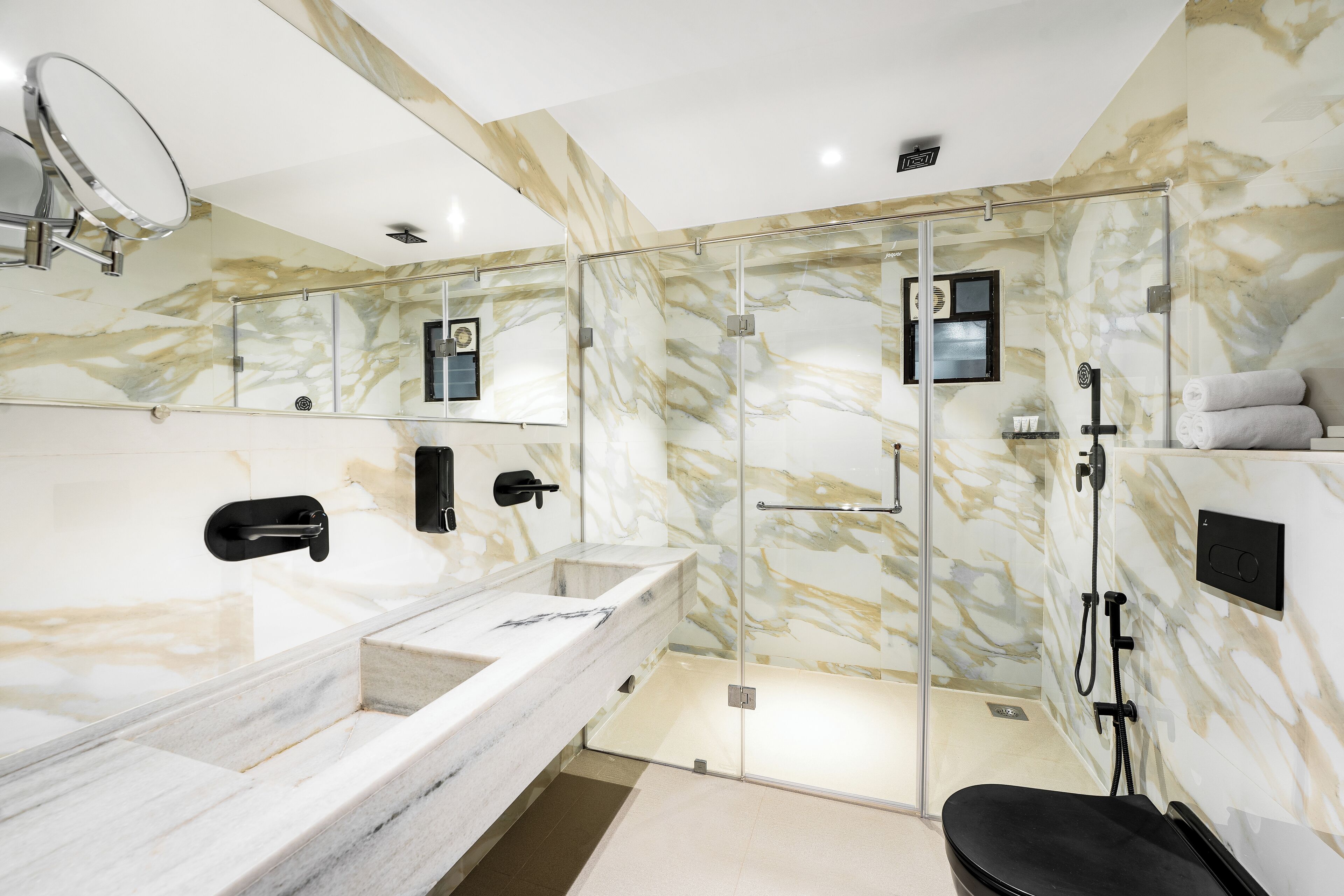Une salle de bain moderne avec un meuble-lavabo en marbre, une douche à parois de verre et des toilettes noires.