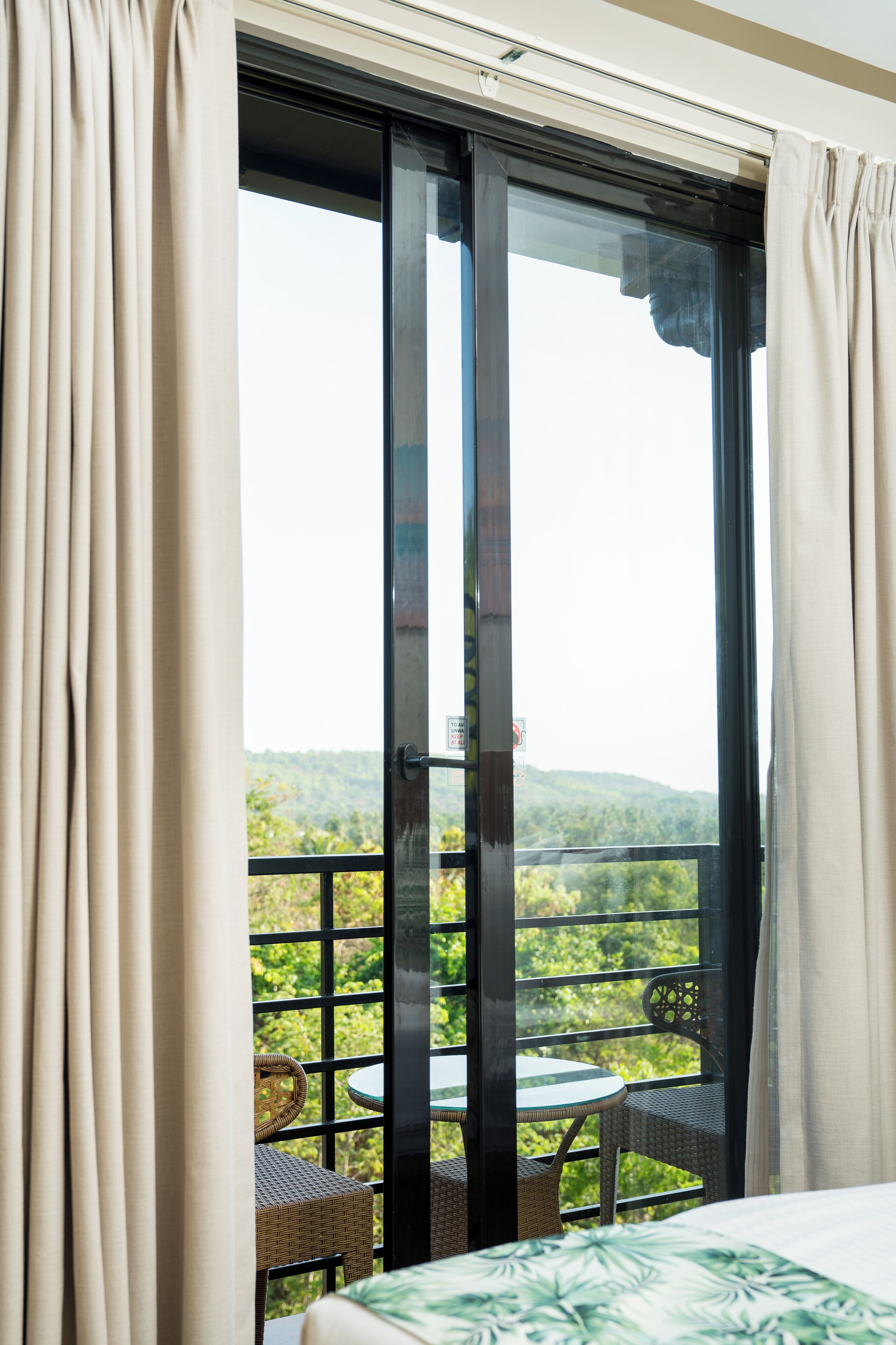 A balcony with wicker furniture and a table, overlooking a green landscape.