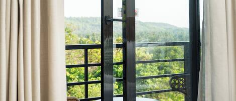Un balcón con mobiliario de mimbre y una mesa, con vistas a un paisaje verde.
