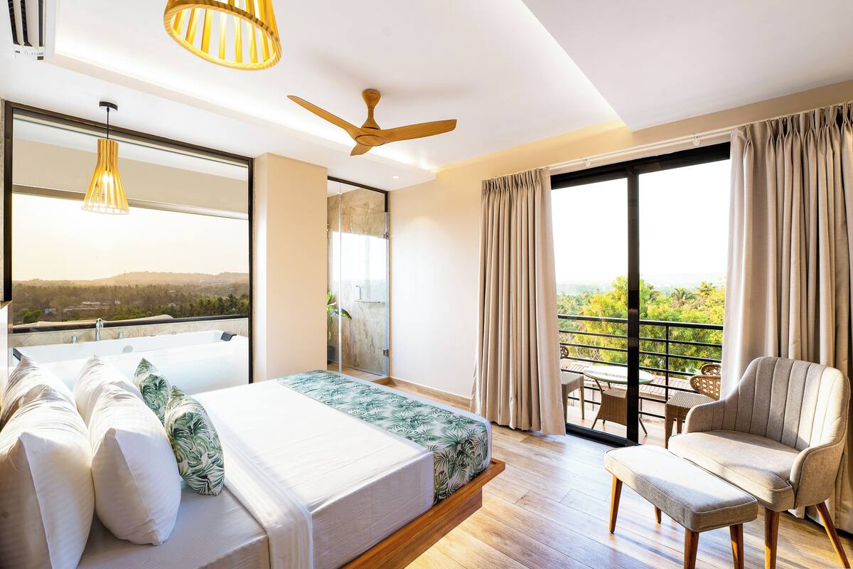 Habitació d'hotel moderna amb un llit gran, zona de seients, un balcó amb vistes i un ventilador de sostre.