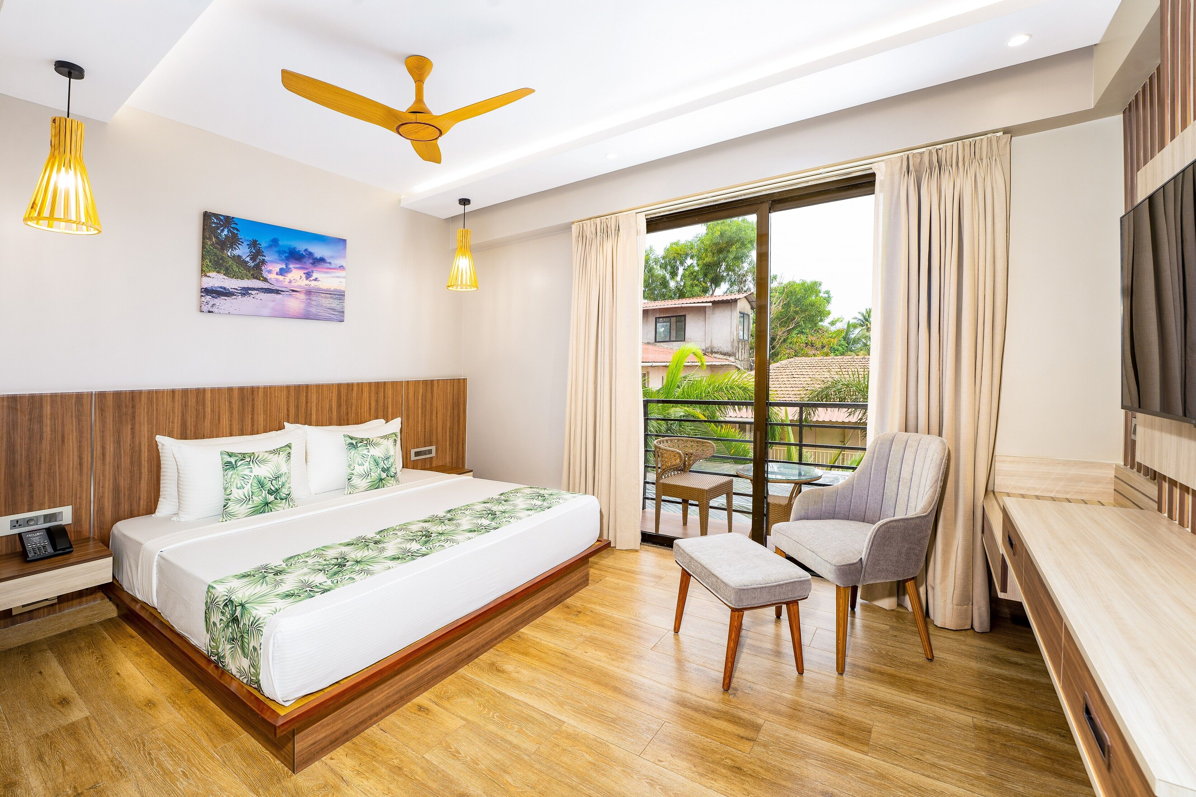 Een moderne hotelkamer met een groot bed, een plafondventilator, een balkon met stoelen en een schilderij aan de muur.