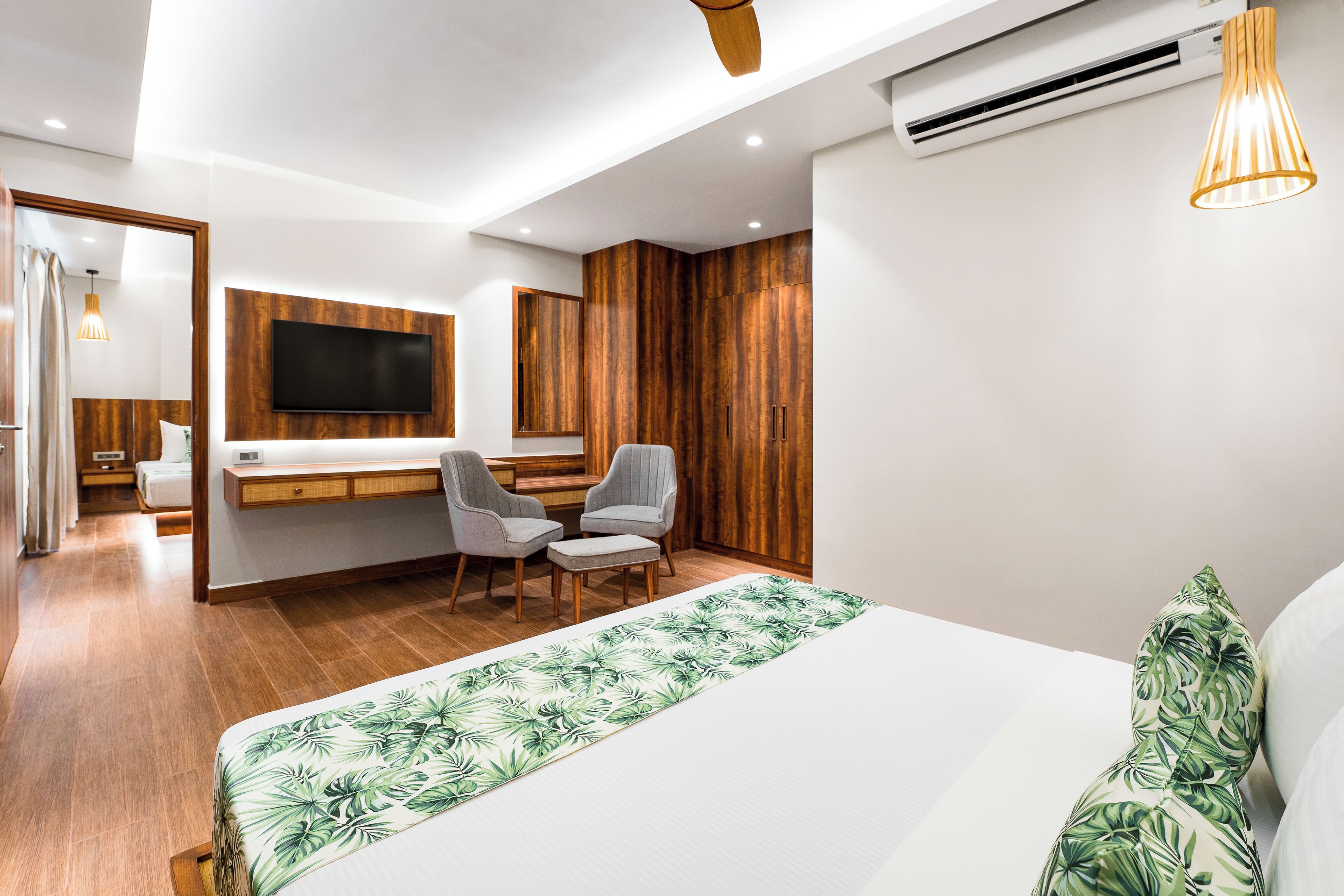 Une chambre moderne avec un grand lit, un bureau avec deux chaises, un téléviseur fixé au mur et un lambris en bois.