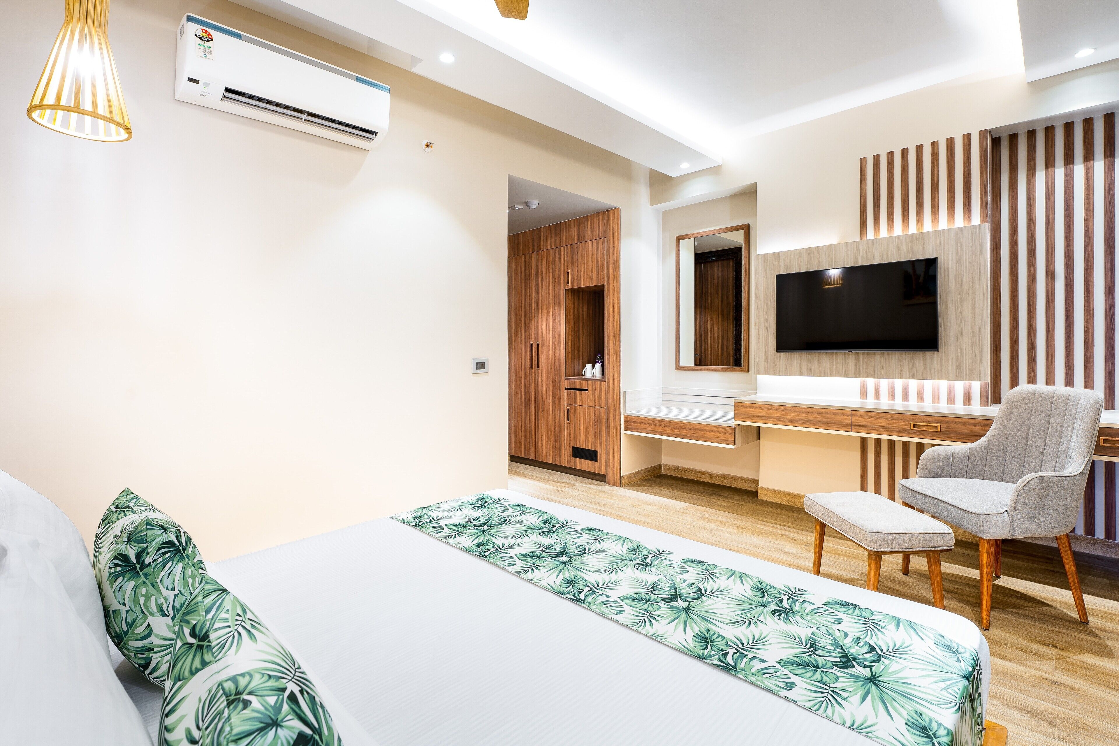 A modern bedroom with a bed, a desk, a chair, a TV, and an air conditioning unit.