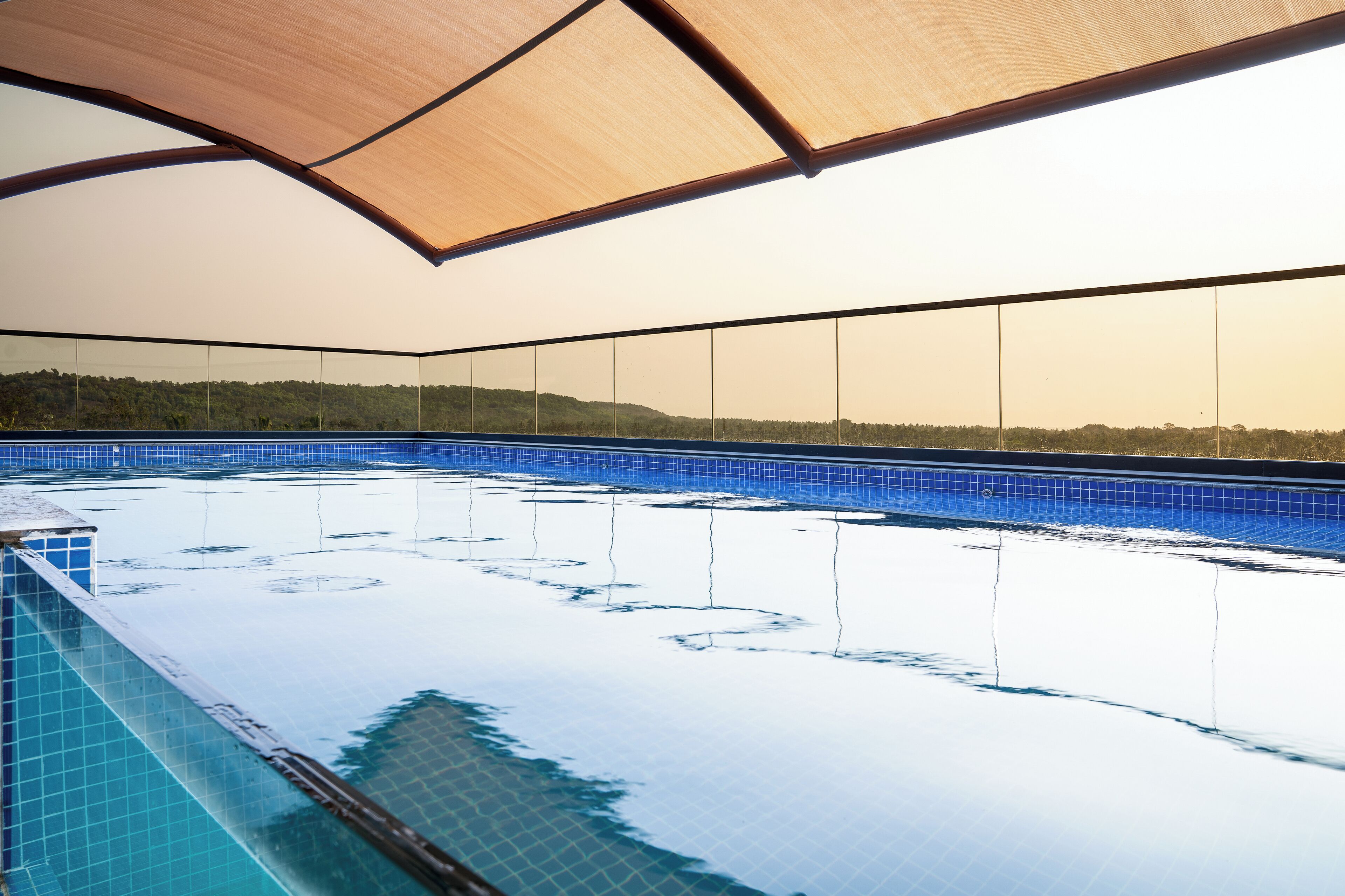An indoor swimming pool with clear blue tiles, a wooden ceiling, and a view of a forested hillside.