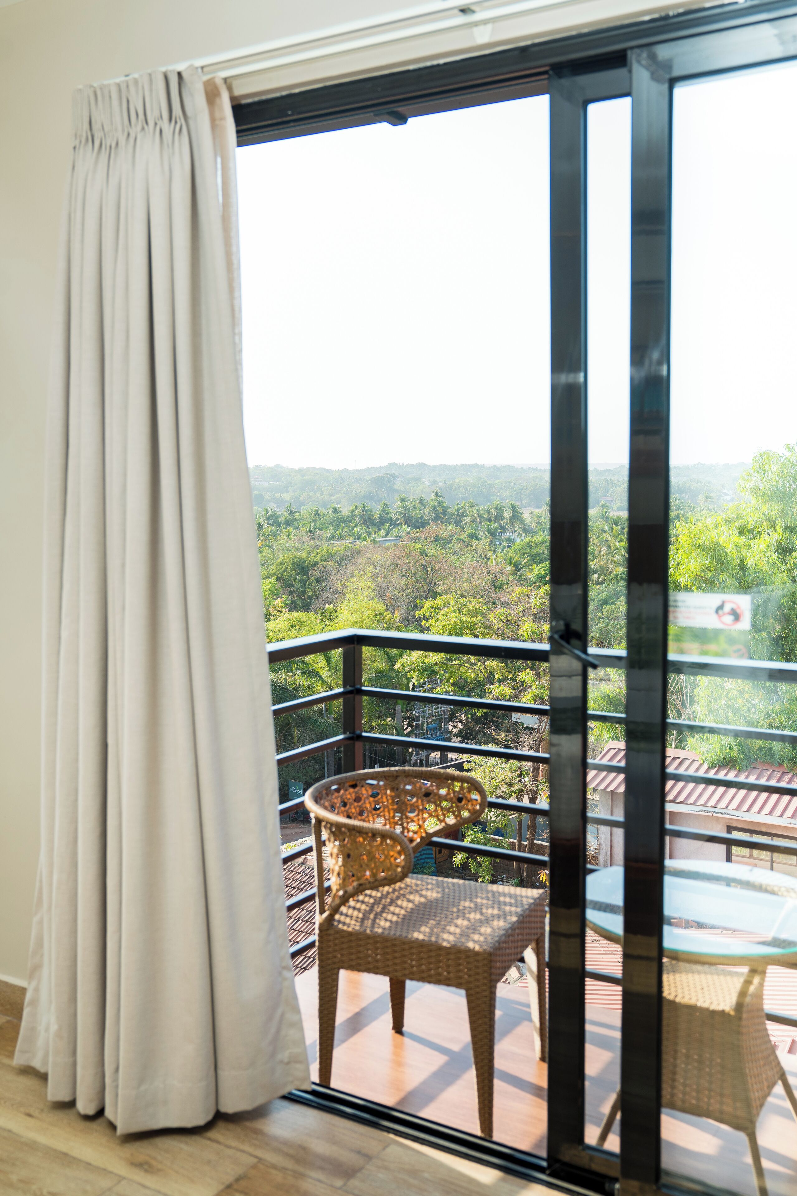 A balcony with wicker furniture, a glass door, and a view of a green landscape.