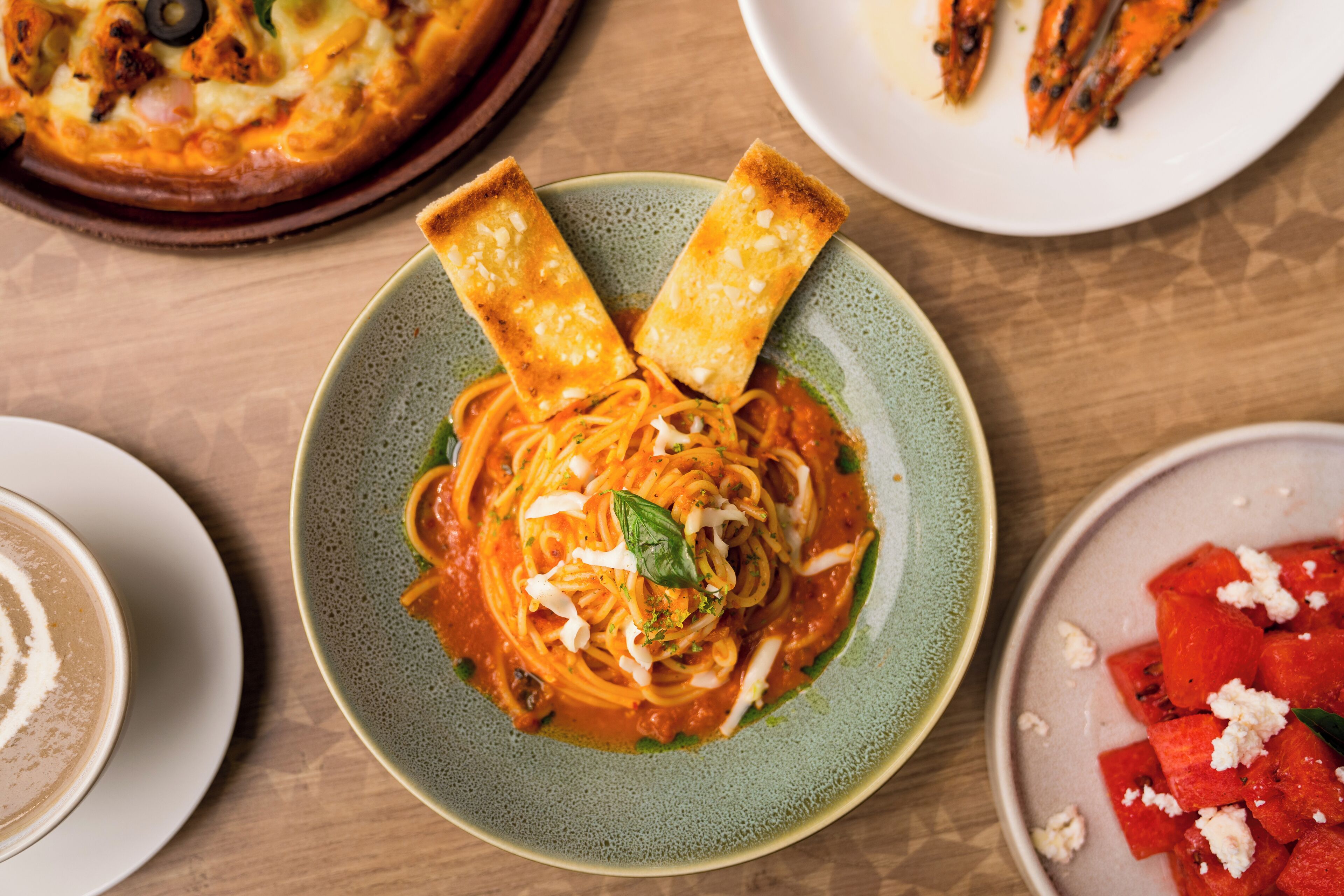 A plate of spaghetti with tomato sauce, garnished with basil and cheese, surrounded by other dishes.