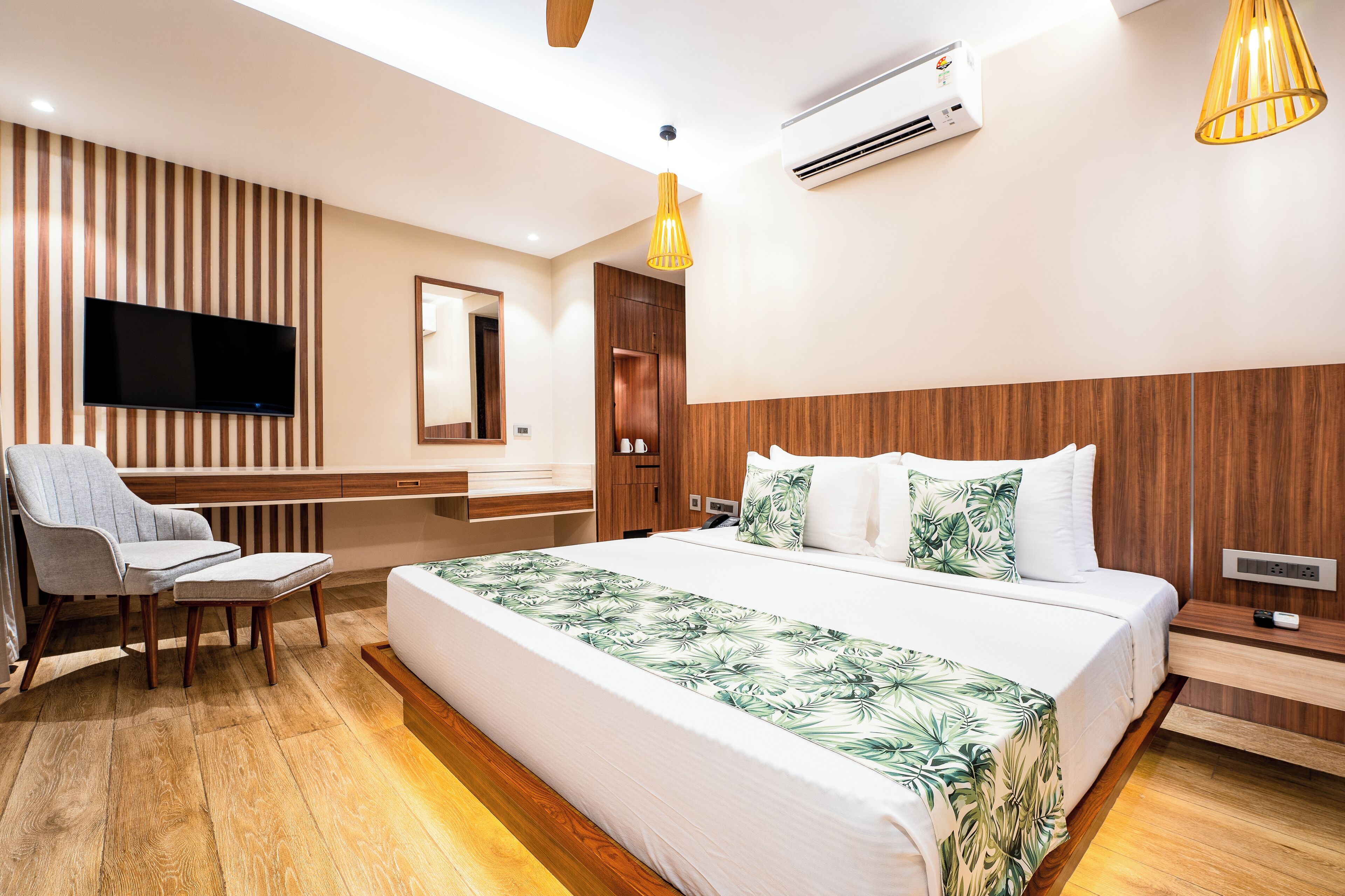 A modern hotel room with a large bed, a TV, a wooden headboard, a desk, and a chair.