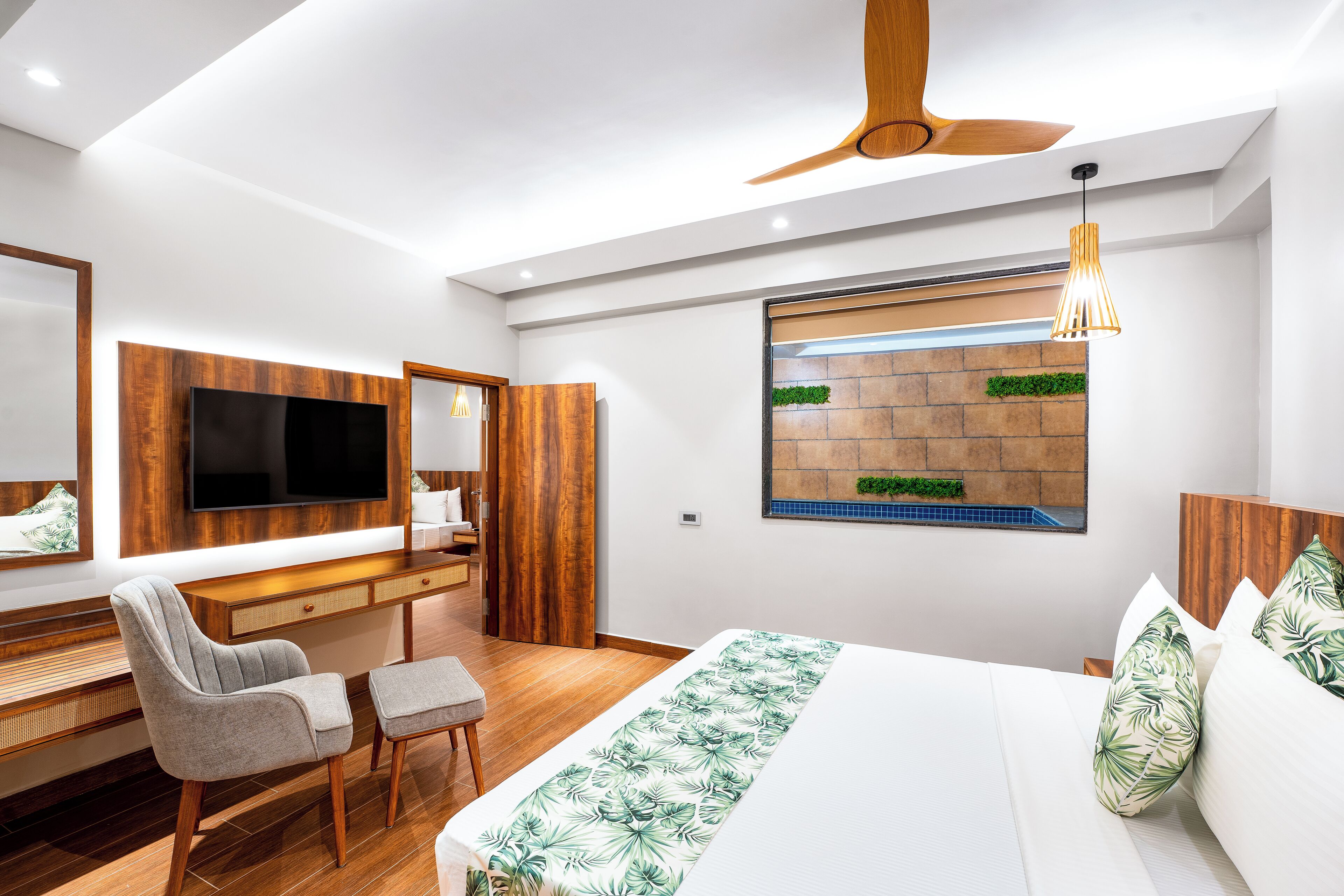 Ein modernes Schlafzimmer mit einem großen Bett, einem Schreibtisch, einem Sessel, einem Fernseher und einem Deckenventilator.