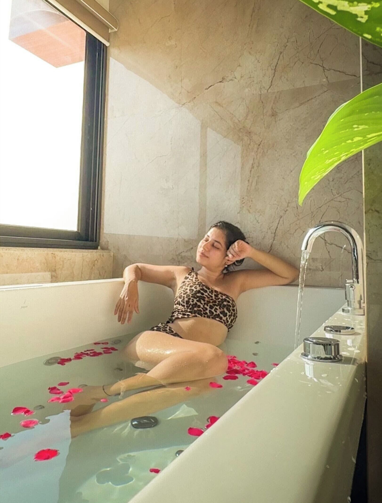 A woman relaxing in a bathtub filled with water and rose petals.