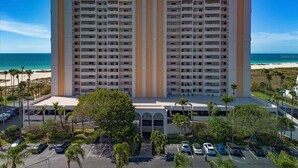 A high-rise hotel with multiple balconies, a parking lot, and a view of the beach.