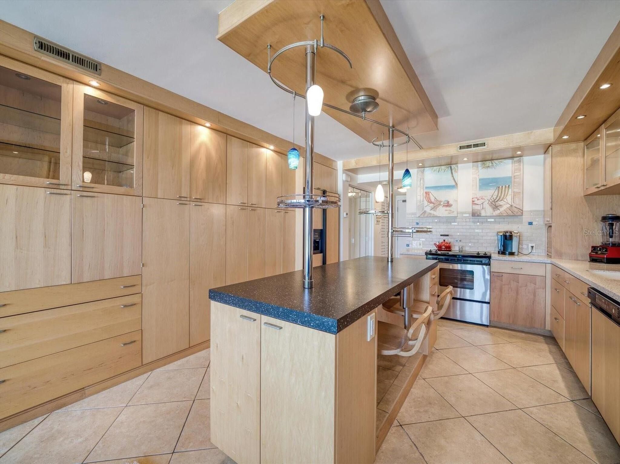 Een moderne keuken met houten kastjes, een centraal eiland, roestvrijstalen apparatuur en hangende verlichting.