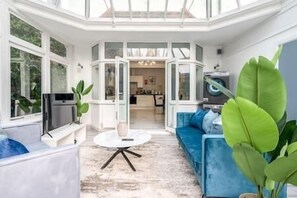 A modern living room with a blue sofa, a round coffee table, and a TV. - The Sterling Room (Harrow)