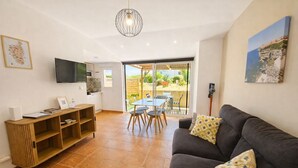 Una sala de estar con un sofá, un televisor, un mueble de madera y un comedor con una mesa y sillas.