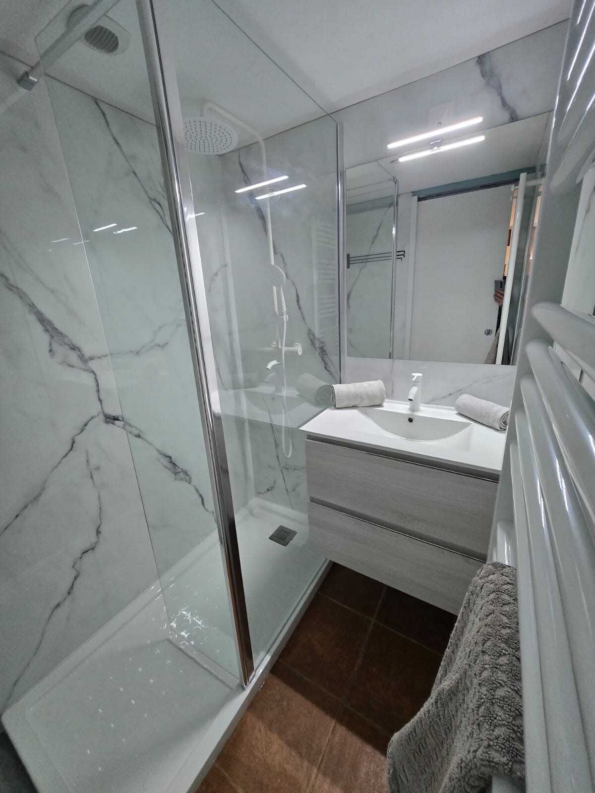 Une salle de bain moderne avec une douche à parois de verre, un lavabo blanc et un miroir au-dessus du meuble-lavabo.