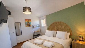 Habitación de hotel con cama, televisión, estante, un cuadro y lámpara.
