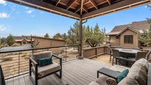 Terraza cubierta al aire libre con asientos y una mesa, con vistas a una zona residencial y árboles.