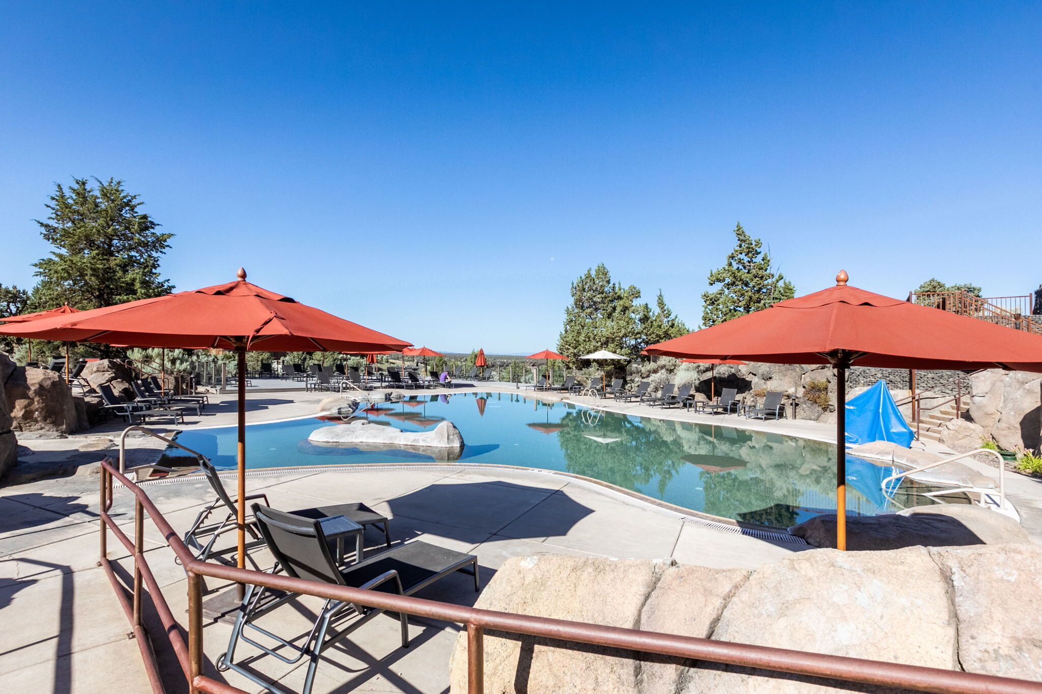 A pool area with red umbrellas, lounge chairs, and a clear blue sky.