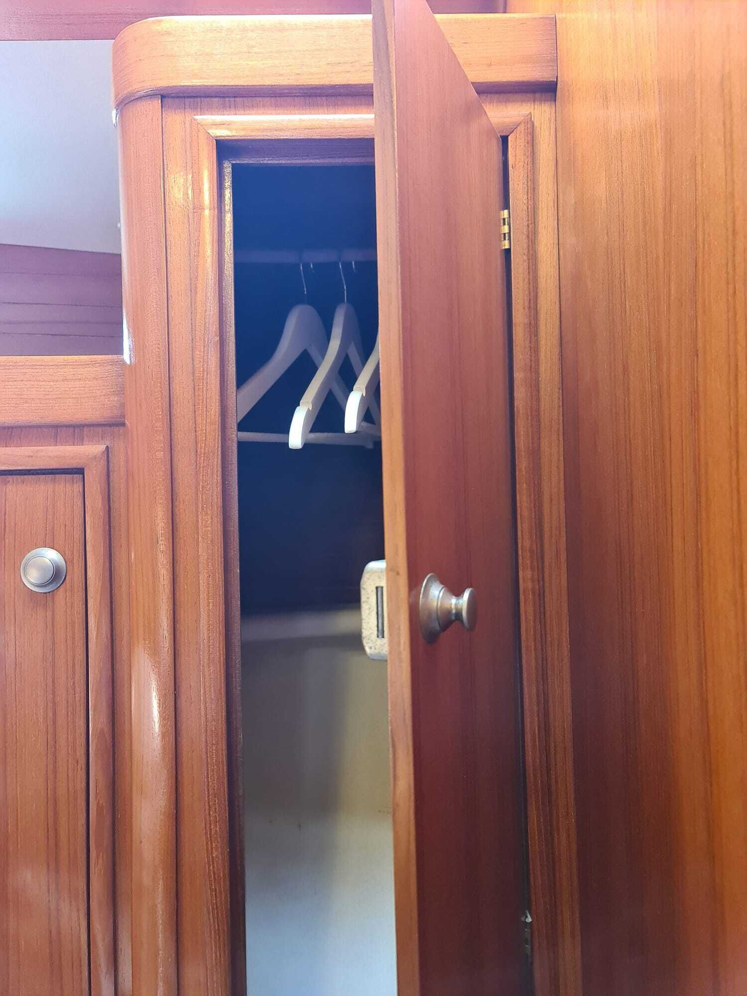 Ein hölzerner Kleiderschrank mit einer teilweise geöffneten Tür, dahinter hängende Kleidung.