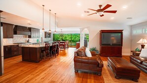 A spacious kitchen with wooden cabinets and a dining area. There is a large flat-screen TV and a ceiling fan. - Private Riverfront Home - 1 mile to the Beach (Bonita Springs)