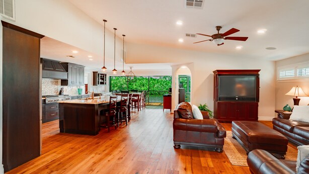 A spacious living area with a wooden floor, a dining area, a kitchen with dark cabinetry, and a large TV. - Private Riverfront Home - 1 mile to the Beach (Bonita Springs)