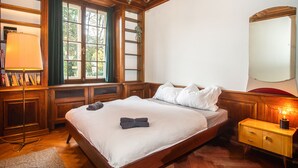 Une chambre avec un grand lit, une table de chevet avec une lampe, un miroir et une fenêtre donnant sur un paysage verdoyant.
