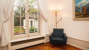 Une pièce avec une grande fenêtre, une chaise, une lampe et un tableau au mur.