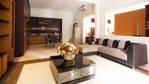 A modern living room with a sofa, a coffee table with a vase, a bookshelf, and a dining area. - Omah Demak Ijo By Occupied  (Sleman)