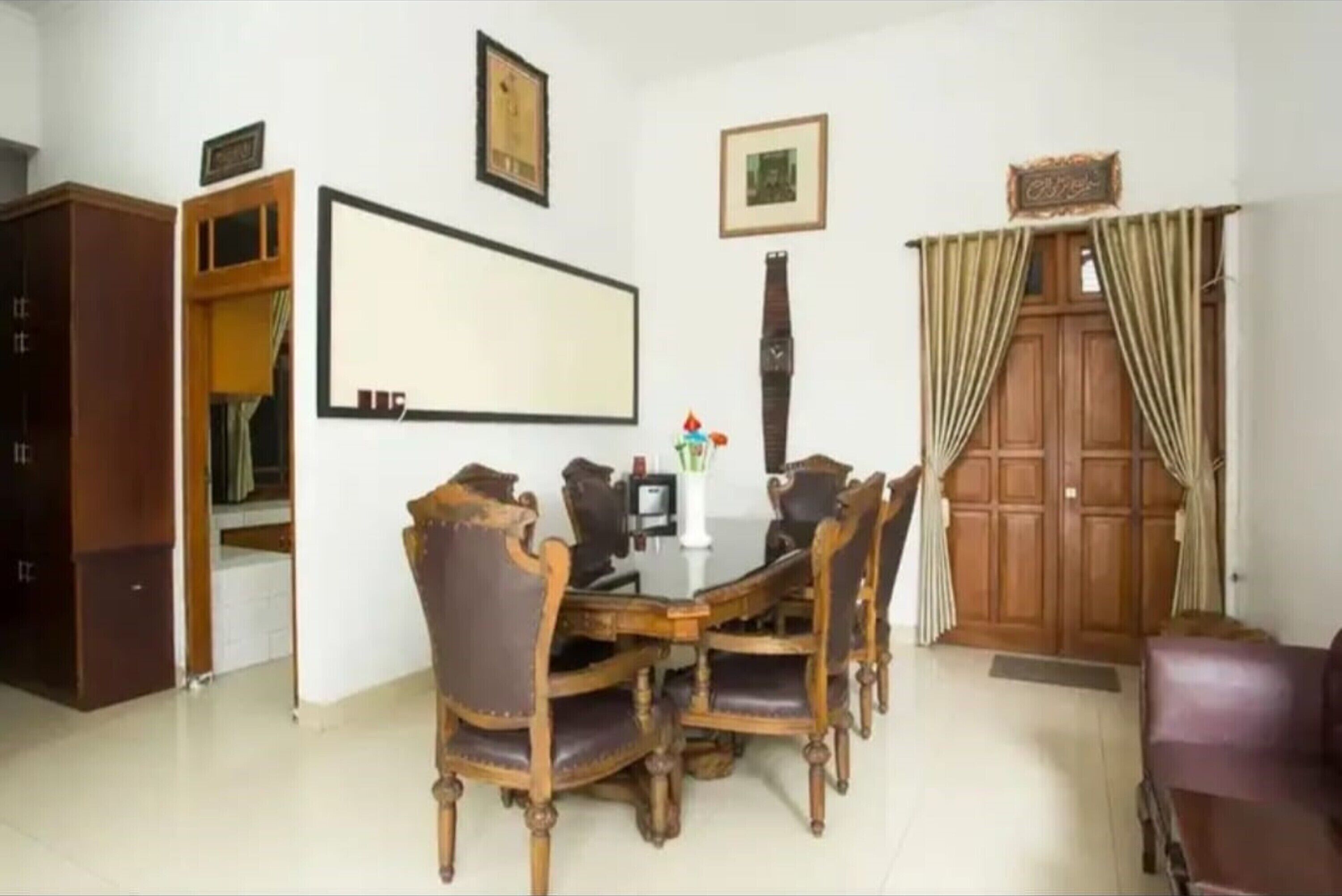 A dining area with a wooden table and chairs, a clock on the wall, and a wardrobe.