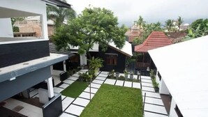 A modern building with a flat roof, a small courtyard with a lawn, and a view of the sea. - Omah Demak Ijo By Occupied  (Sleman)