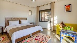 A bedroom with a large bed, a sofa, a small table with a vase of flowers, and a window with curtains. - Villa Leila Farmhouse  (marrakech)