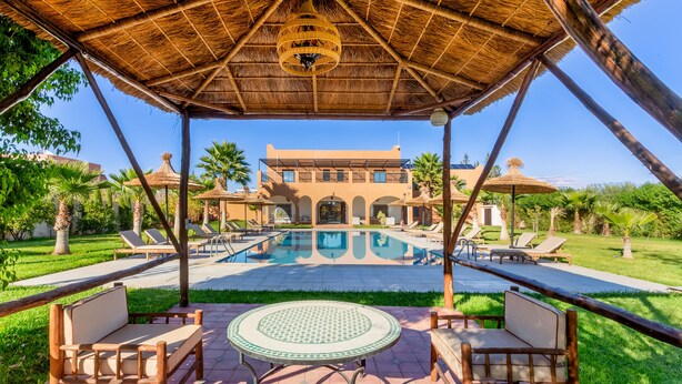 A poolside area with lounge chairs, a table, and a thatched roof structure. - Villa Leila Farmhouse  (marrakech)