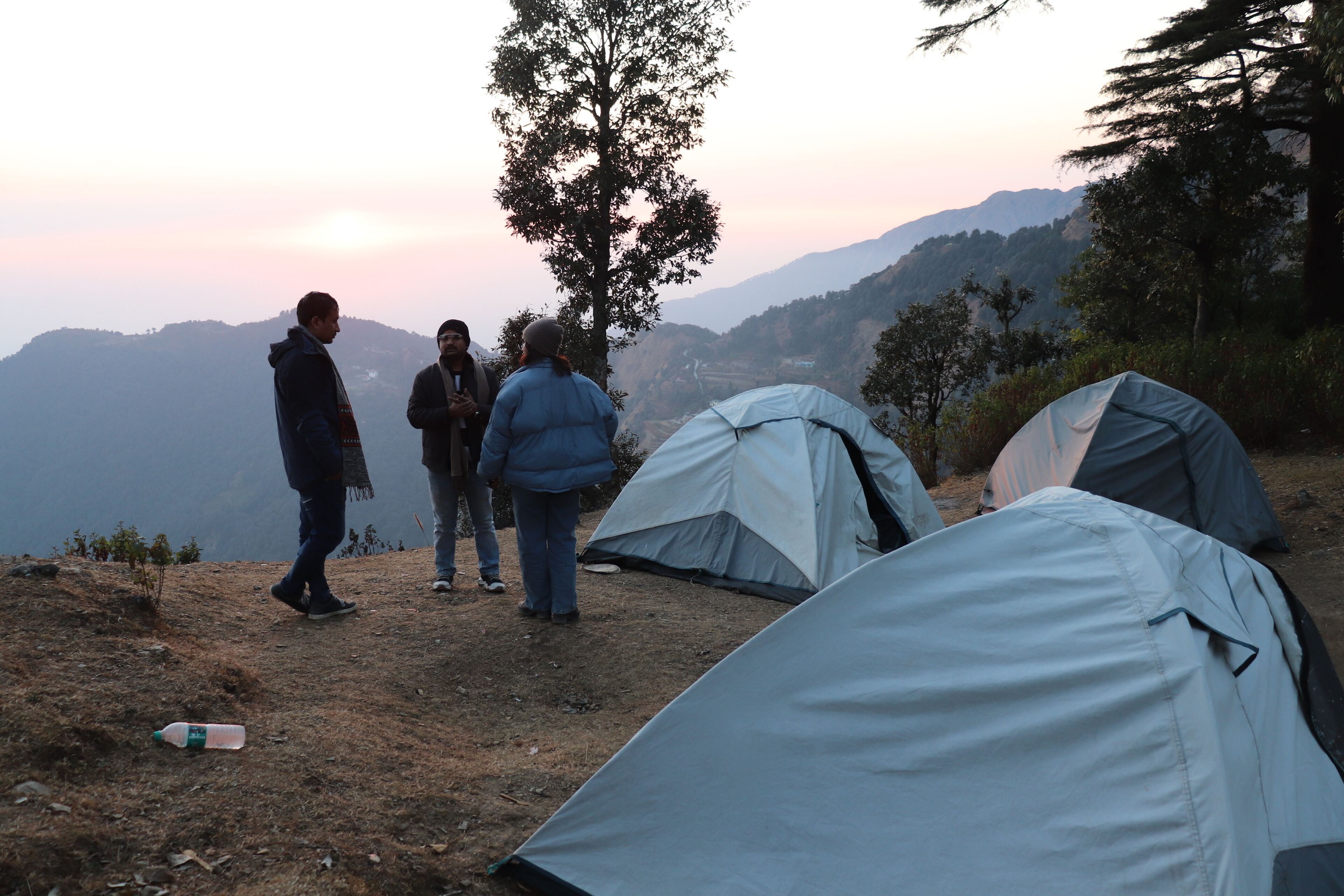 A group of people standing near tents on a hillside with a view of mountains in the background.