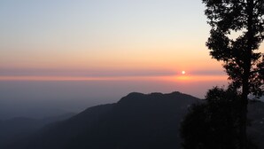 Paisaje montañoso al amanecer con la silueta de un árbol.