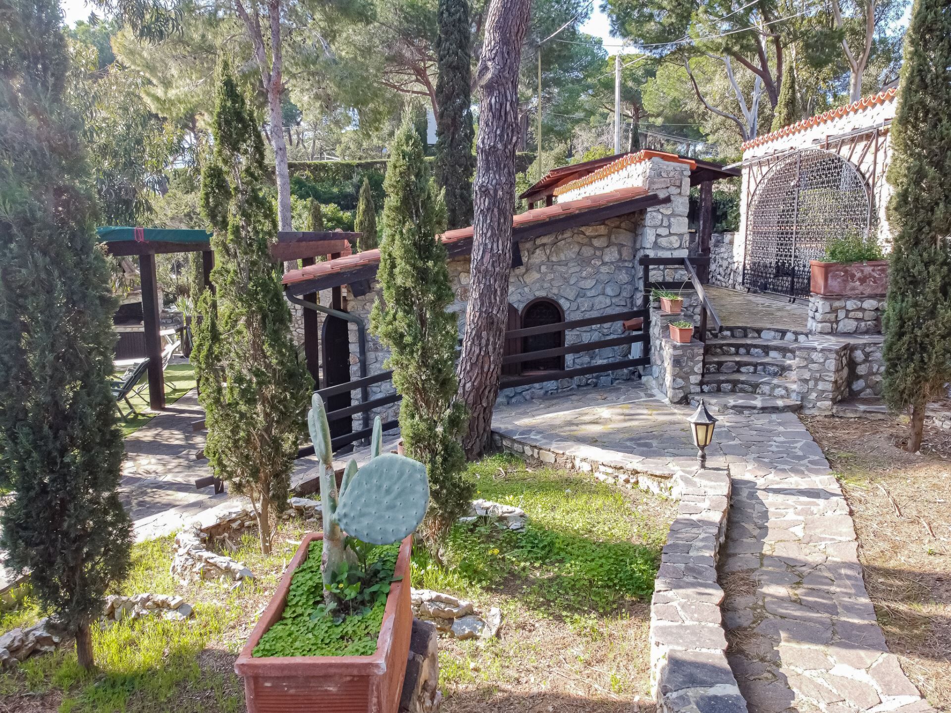 A stone building with a red-tiled roof, surrounded by trees and a stone pathway.