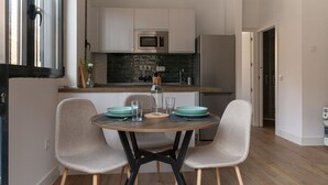 Et moderne køkken med hvide skabe, en mikrobølgeovn og et køleskab. Der er et spisebord med stole og en vase med blomster.