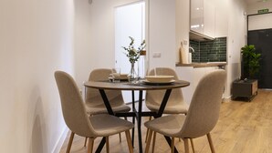 Un coin repas avec une table ronde, quatre chaises, un vase de fleurs et, en arrière-plan, une vue sur une cuisine et une porte.