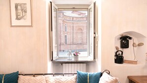 A room with a bed, a window with a view of a building, a telephone, and a small shelf with a kettle and a sign. - ROYAL HOUSE on the Palace of Venaria (Venaria Reale)