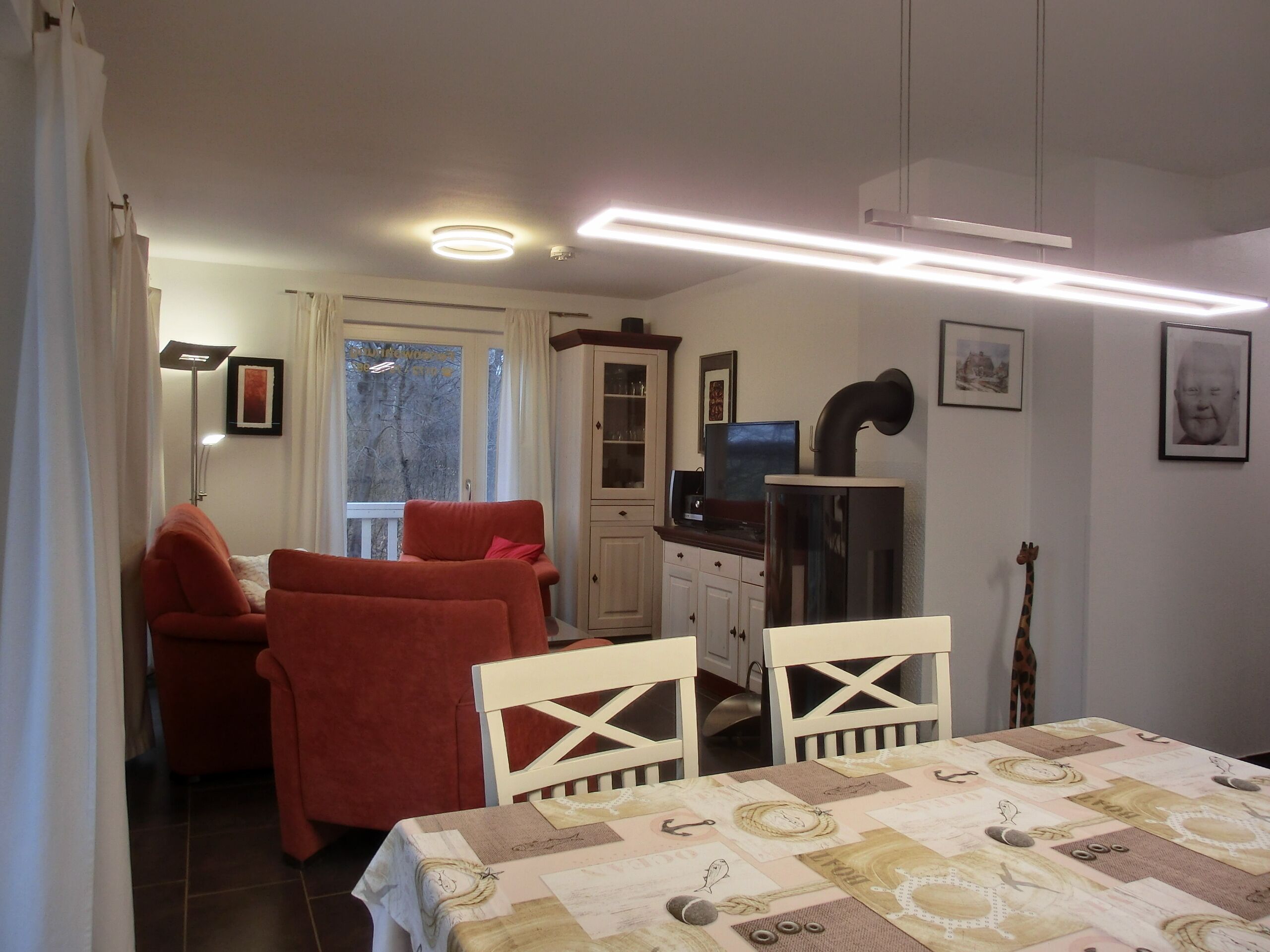 A room with a dining table, two red chairs, a television, and a cabinet.