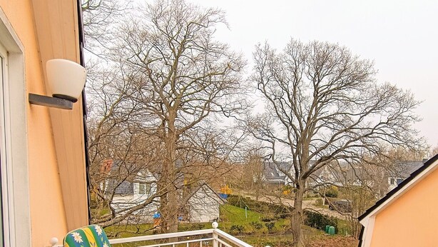 Ein Balkon mit zwei Stühlen und einem Tisch, der auf einen Wohnbereich mit Häusern und Bäumen blickt.
