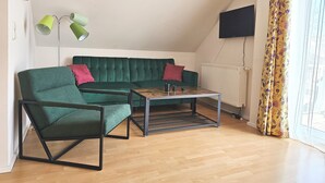 Ein Wohnzimmer mit einem grünen Sofa, einem grünen Sessel, einem Couchtisch, einer Stehlampe und einem Fernseher.