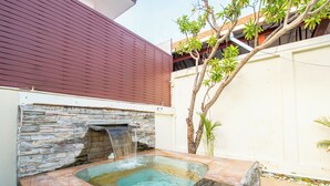Un jacuzzi con caída de agua, paredes de piedra y un árbol.