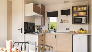 Cocina compacta con estufa, lavamanos y microondas. Hay armarios y una ventana con vistas al verdor.