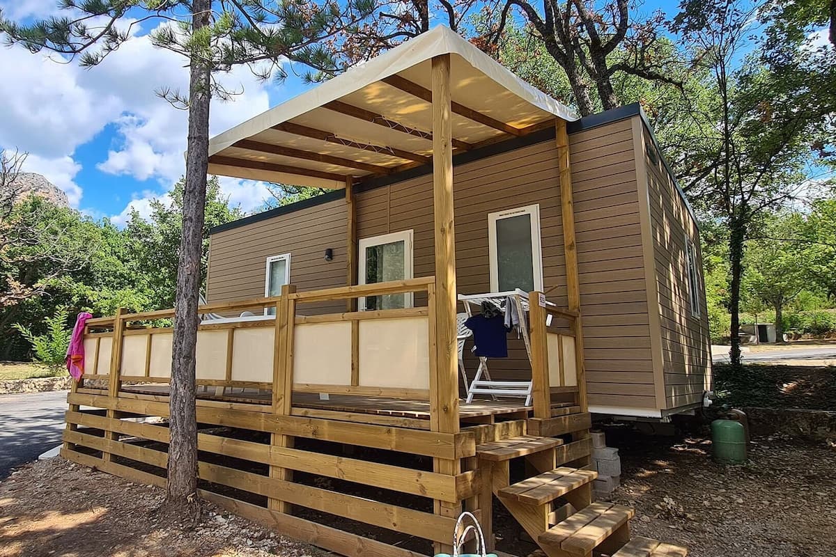 Een klein houten huisje met een veranda, een klein bijgebouw en een overdekt terras.