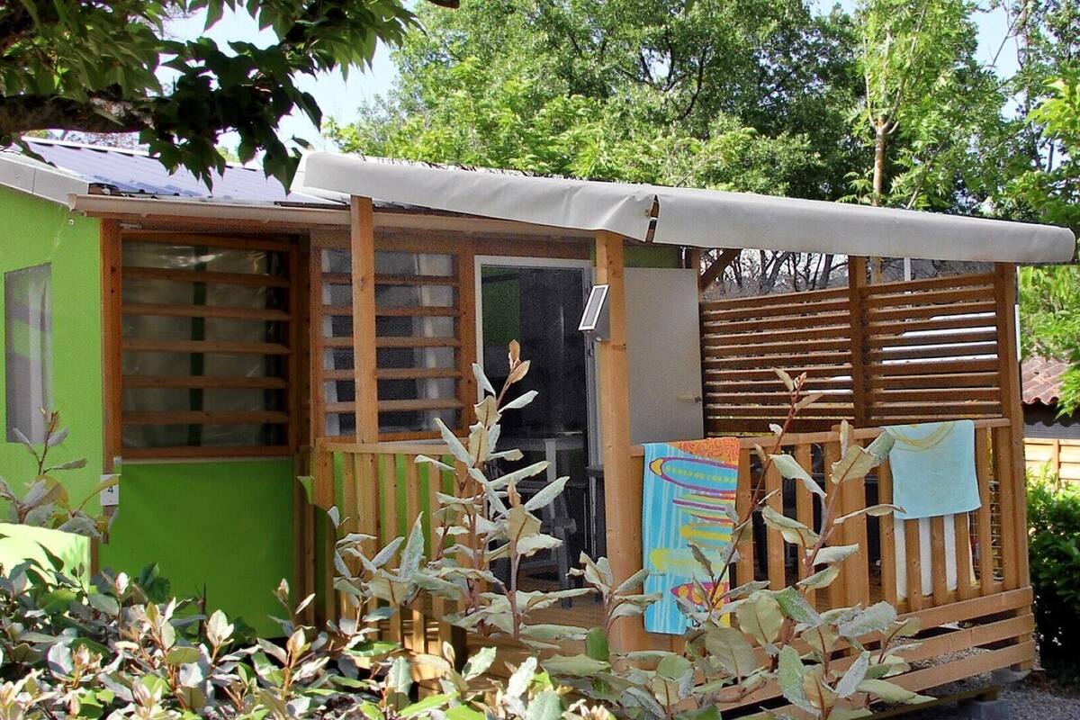 Een klein, gelijkvloers gebouw met een groene gevel, een houten terras en een overdekte veranda.