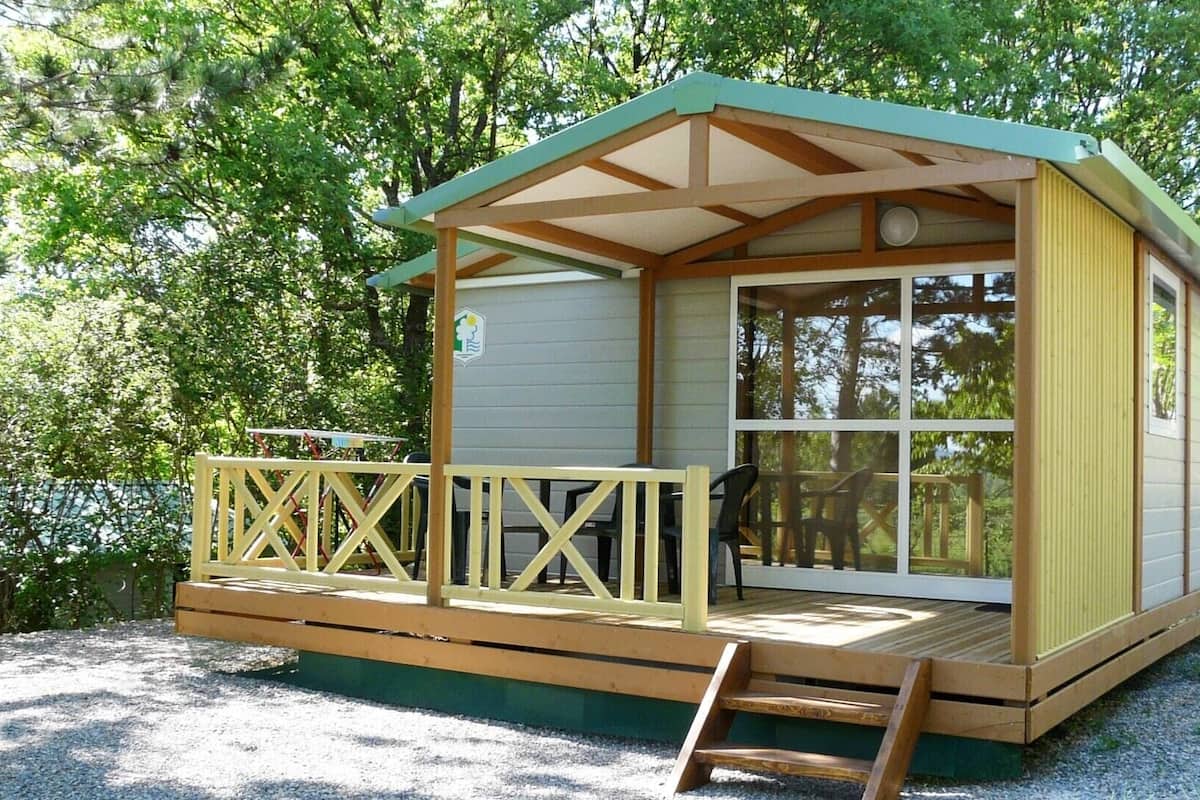 Een klein huisje met een houten terras, een overdekte veranda en grote ramen.