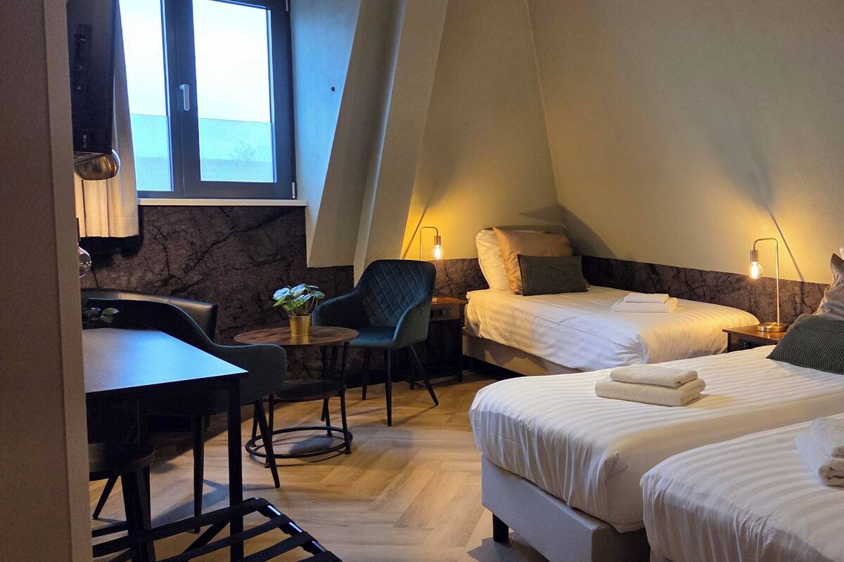 Habitación de hotel con dos camas, un escritorio, una silla y una mesita.