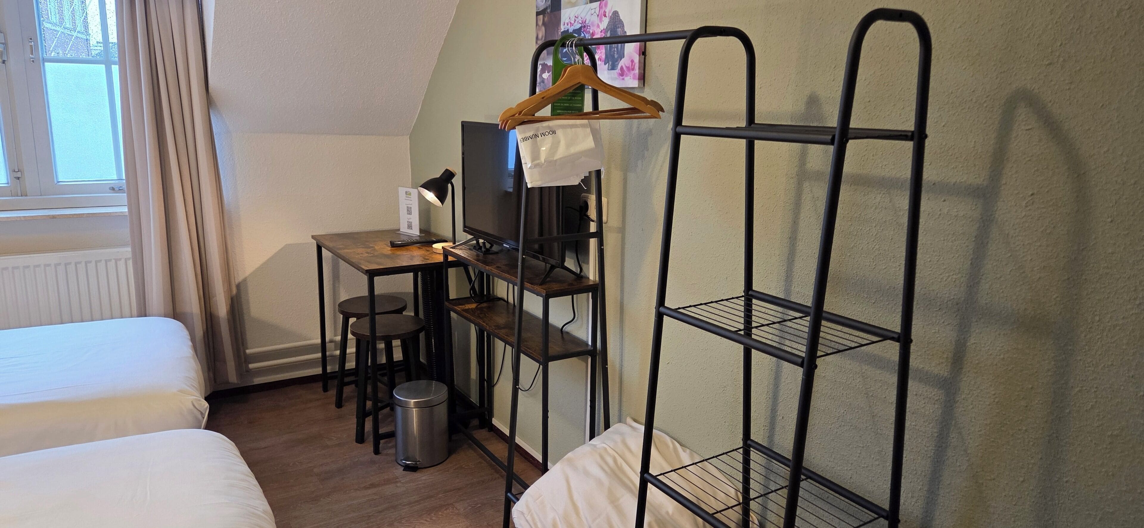 A room with a bed, a desk with a computer, a chair, a hanging shelf, and a radiator.