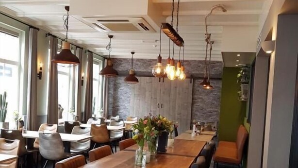 A modern dining area with a long wooden table, leather chairs, and pendant lighting. - Hotel 't Trefpunt (Made)