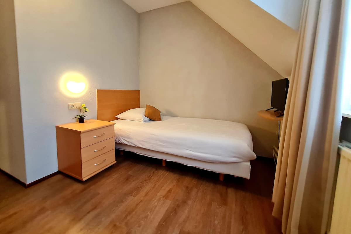 Un dormitorio con cama, mesita de noche, lámpara y televisor.