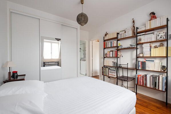 A hotel room with a large bed, a bookshelf, a desk with a lamp, and a window. - Beaugrenelle Skies, by Veeve (Paris)
